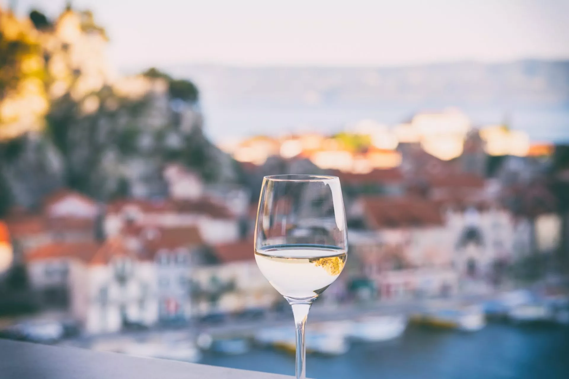 Glas Wein mit Blick auf die Riviera von Omis, entspannende Meereslandschaft im Hintergrund im weichen Licht des Sonnenuntergangs, Dalmatien, Kroatien